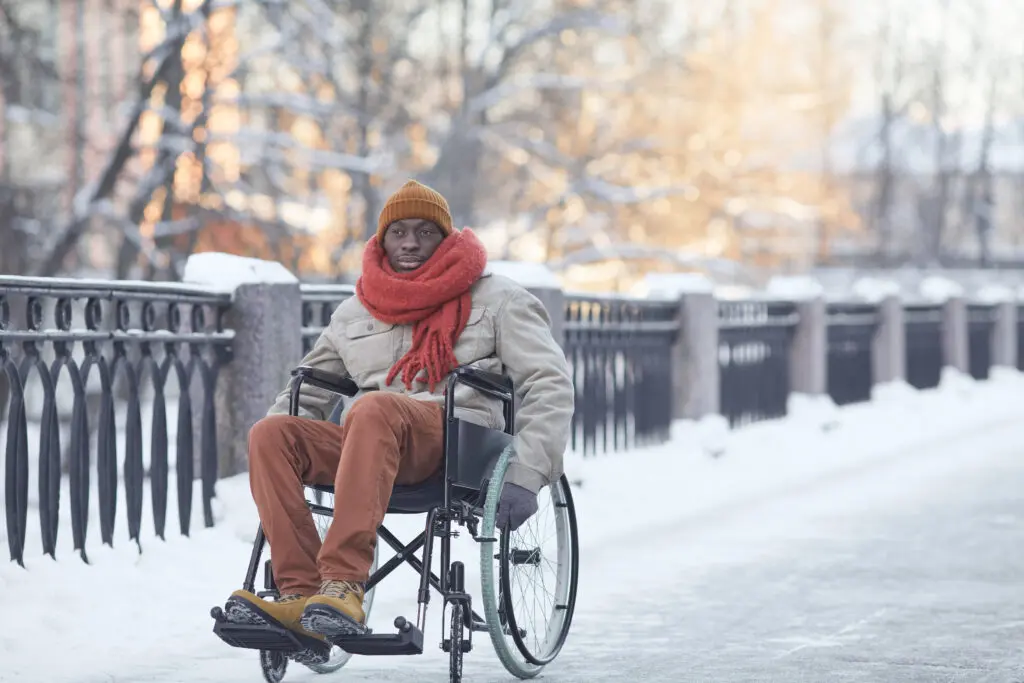 African American man using wheelchair outdoors in winter with snow on the ground.