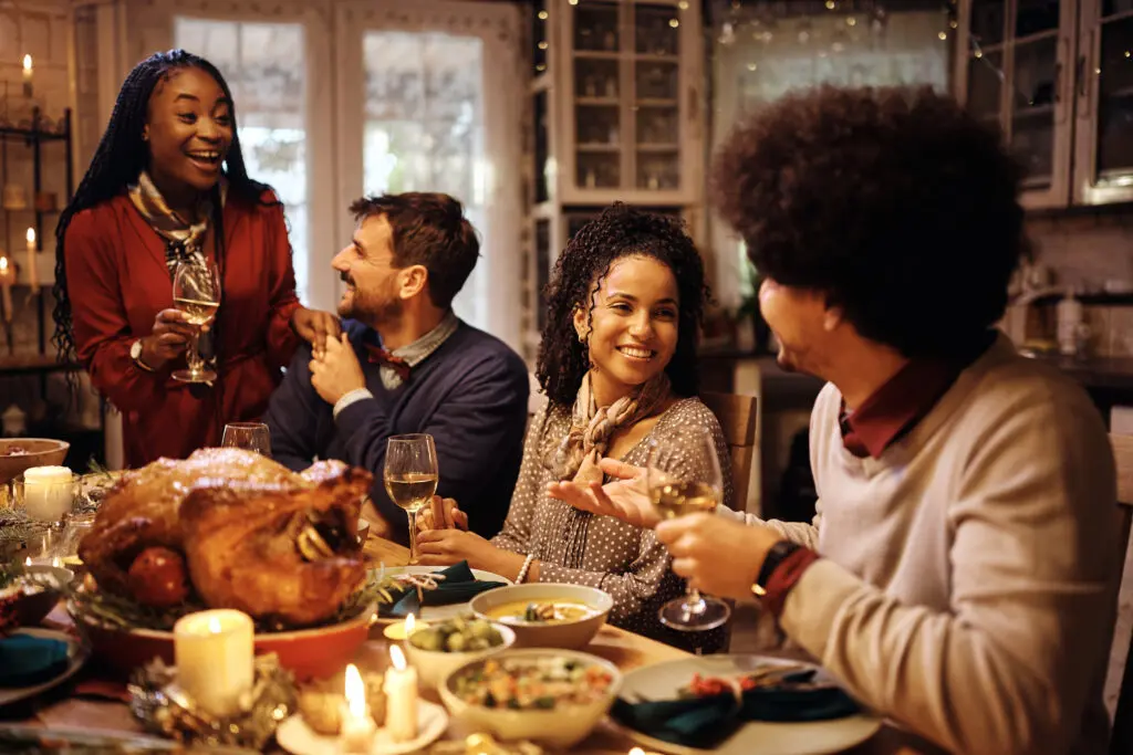 Young happy people talking and drinking wine during Thanksgiving dinner at home.