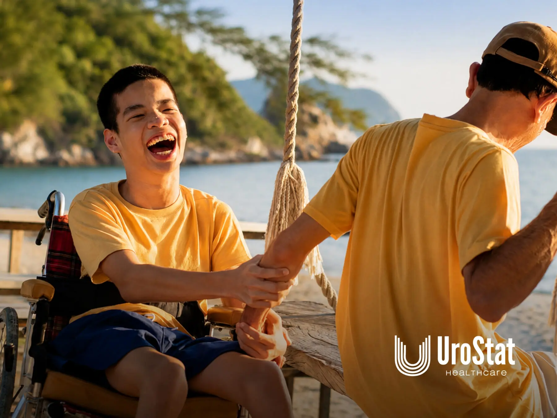 Caregiver holding hands with young man in wheelchair, laughing together outdoors near the coast