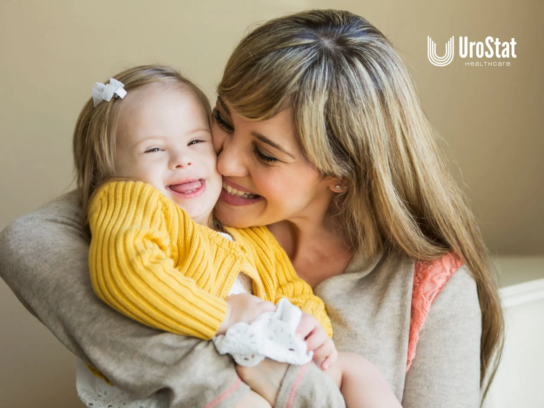 A smiling mother holds her young daughter, who is wearing a yellow sweater and laughing.