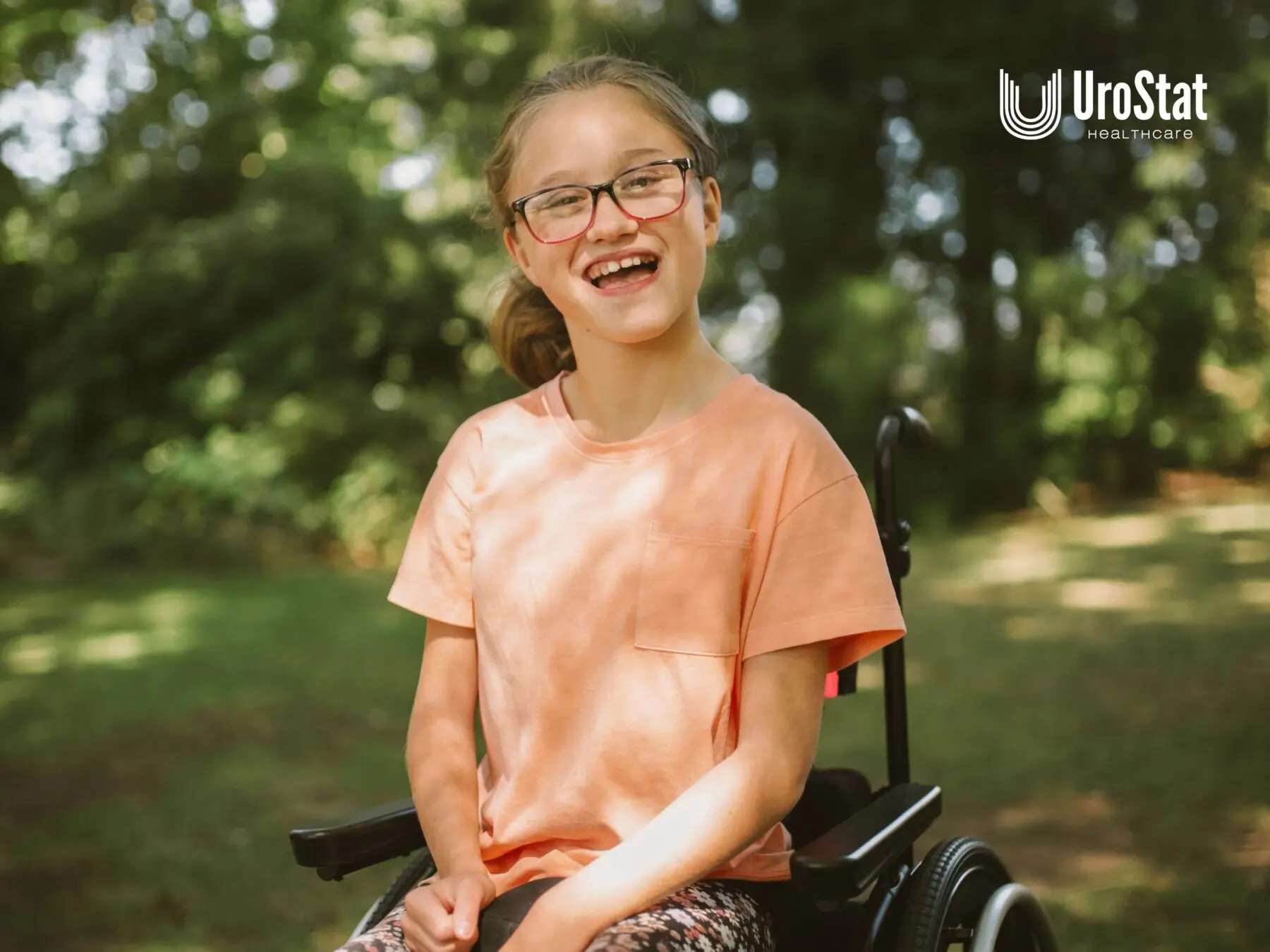 Smiling girl wearing glasses and a peach shirt seated in a wheelchair outdoors