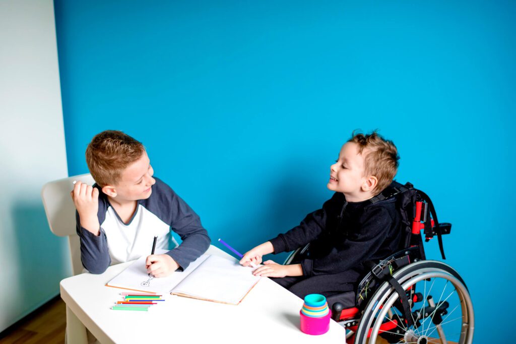 Two boys sitting at table together, one is in a wheelchair due to Spinal Muscular Atrophy..