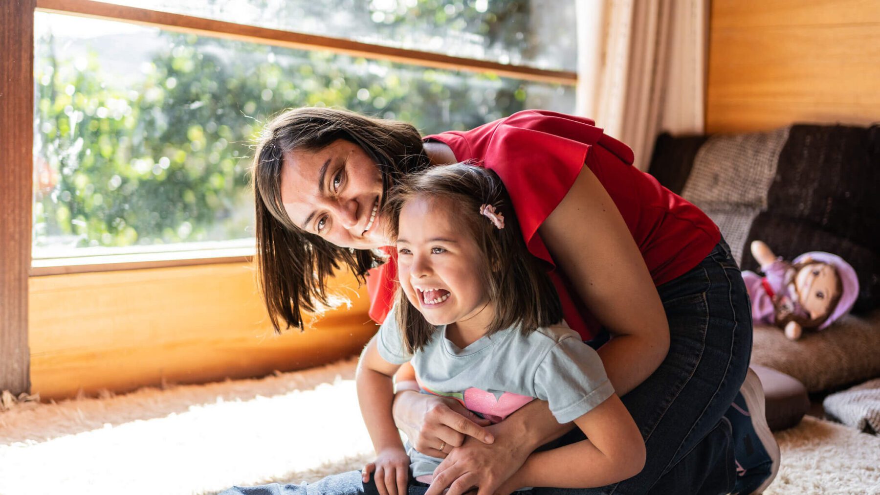 Portrait of mother and daughter playing on living room at home - including child girl with down syndrome