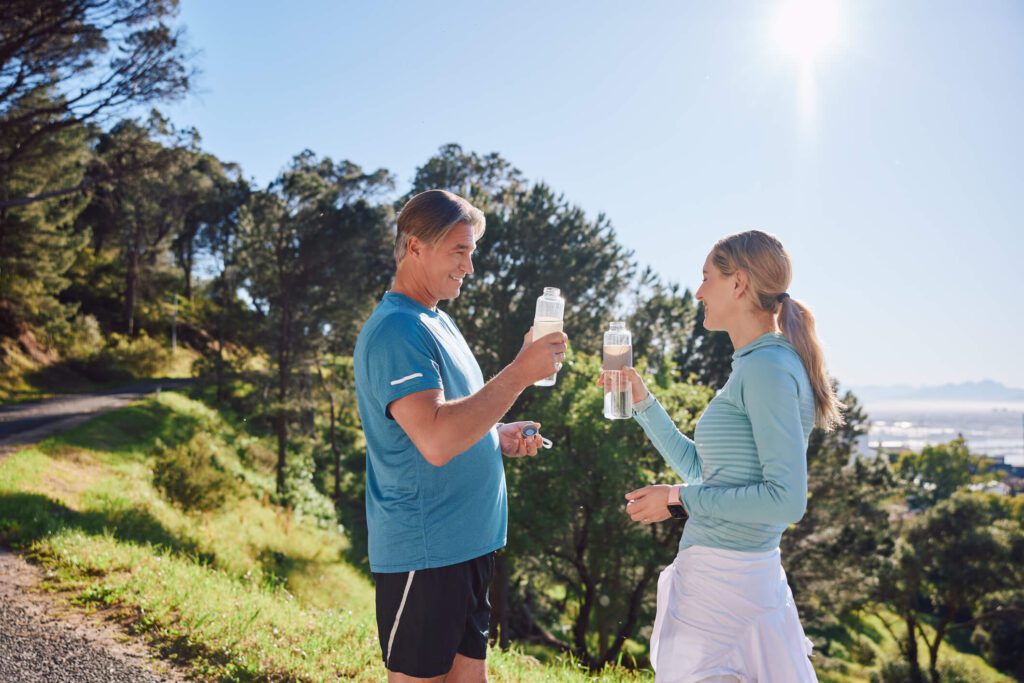 Senior dad and his daughter holding water bottles in nature for a workout break.