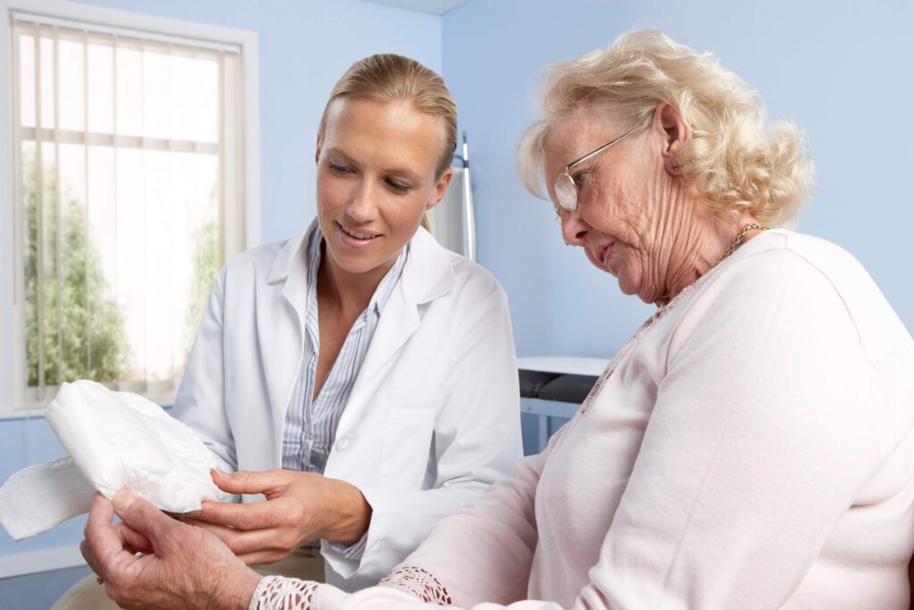 Female doctor with elderly female patient holding urinary incontinence pad.