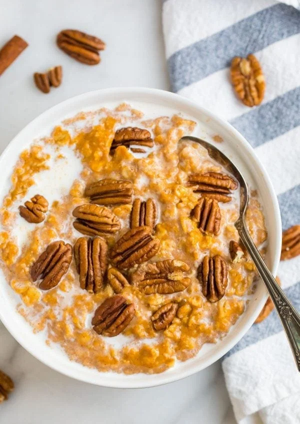 Pumpkin oatmeal in white bowl with walnuts on it, a spoon in it
