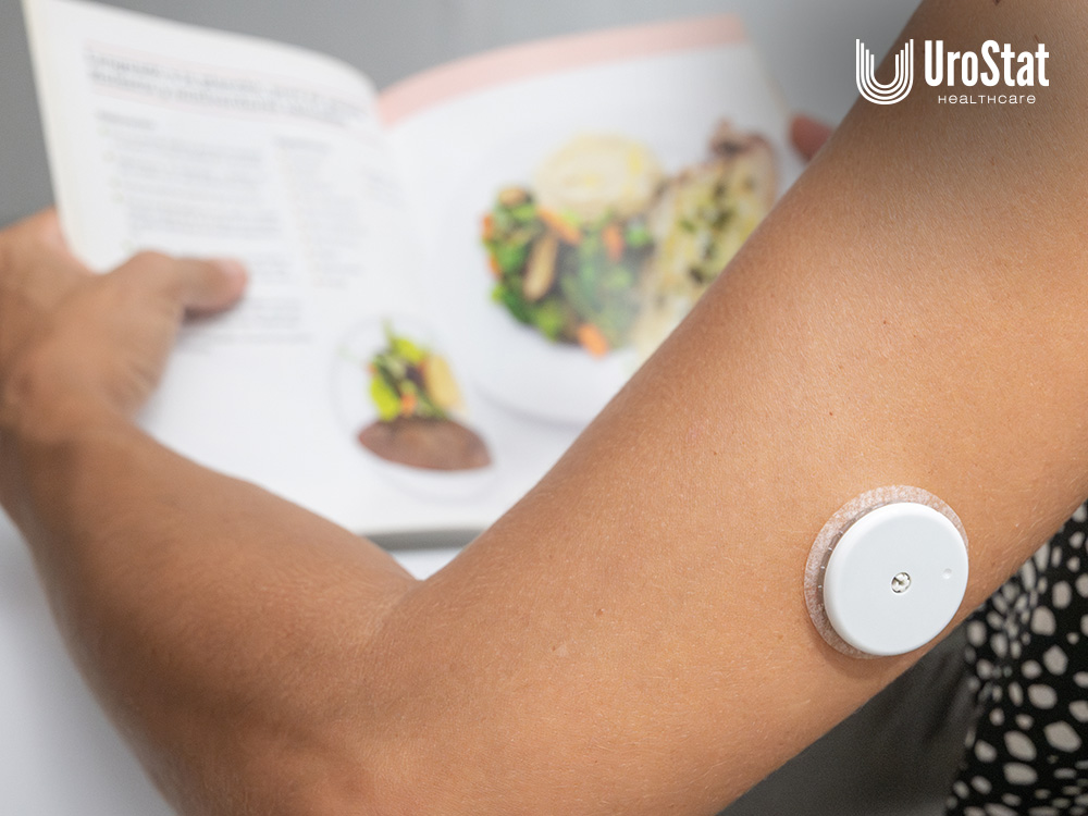Close up of the back of an arm with a CGM device on it with food in the background