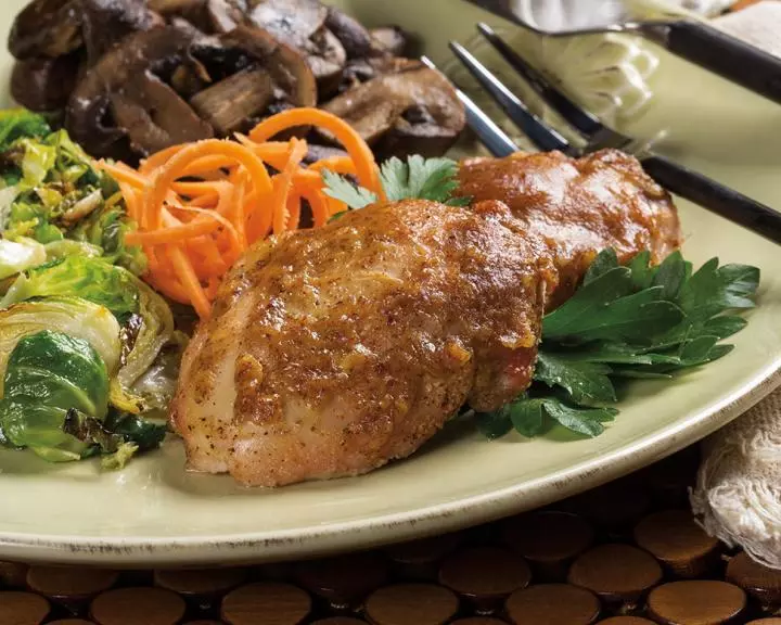Two chicken thighs cooked in maple mustard with carrots, mushrooms, and other greens on a dinner plate