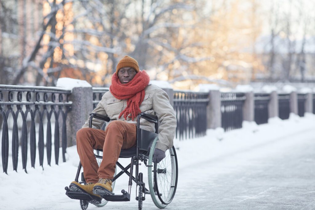 African American man using wheelchair outdoors in winter with snow on the ground.