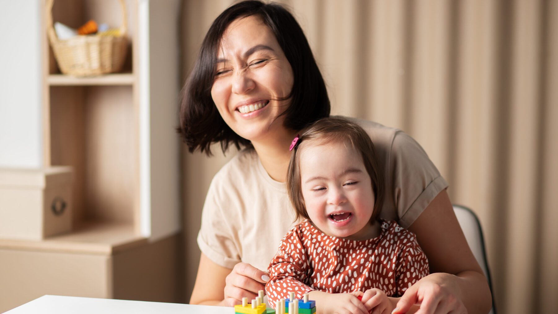 Girl with down syndrome smiling and assembling toy with mom