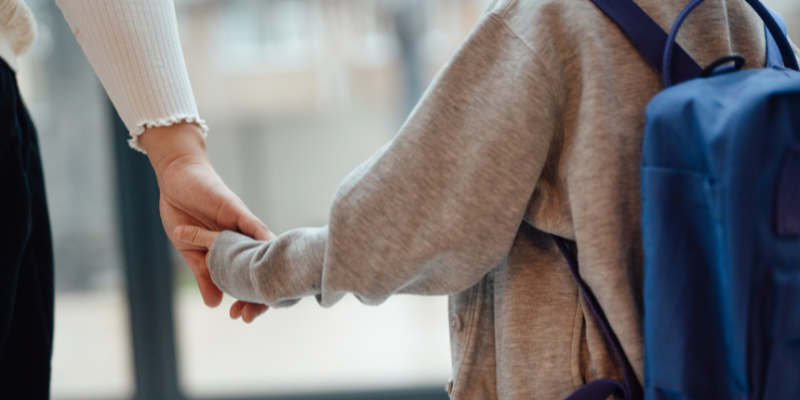 Mother holding hands with child with backpack on