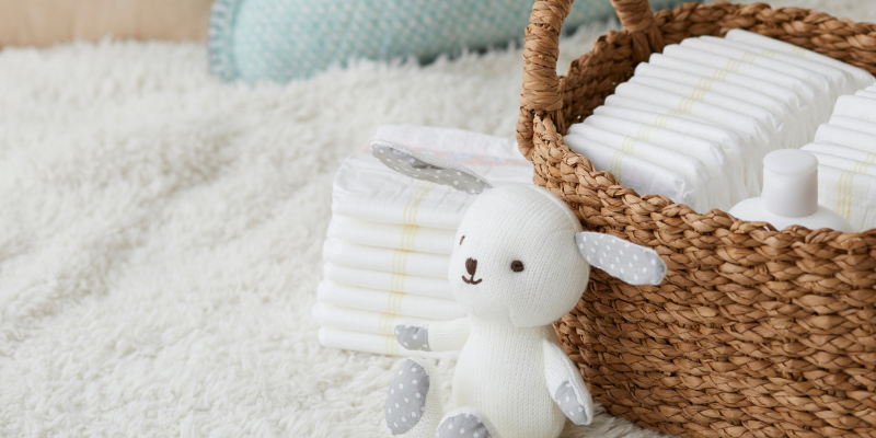 Stuffed dog toy next to wicker basket of diapers with diapers stacked next to it as well