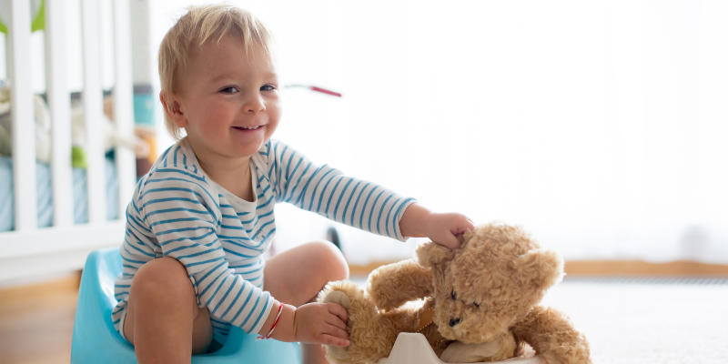 Baby sitting on potty and holding their stuffed bear on the potty next to them