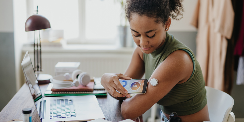 Young girl with CGM on the back of her arm scanning it with smartphone while sitting at her desk