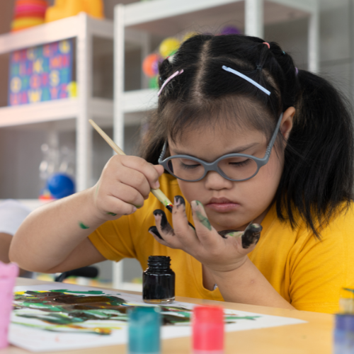 Girl with autism painting on fingers and hand in school