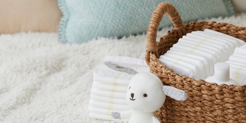 Diapers in a woven basket with small stuffed animal in front of it