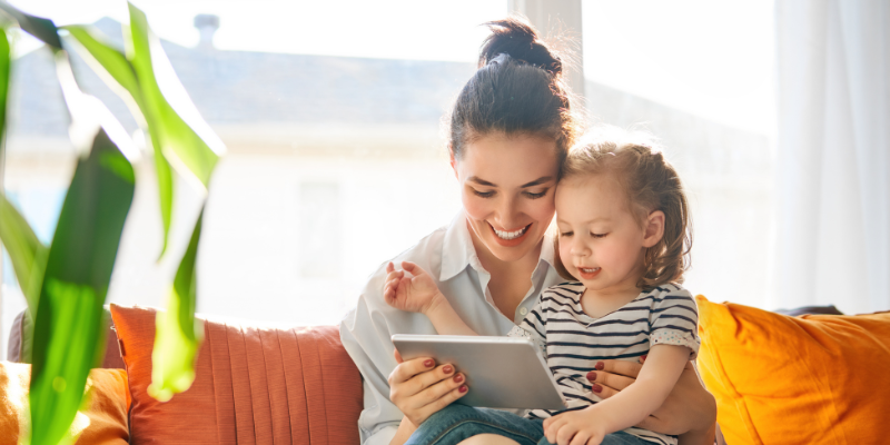 Mom sitting on the couch with her daughter in her lap looking at a tablet together