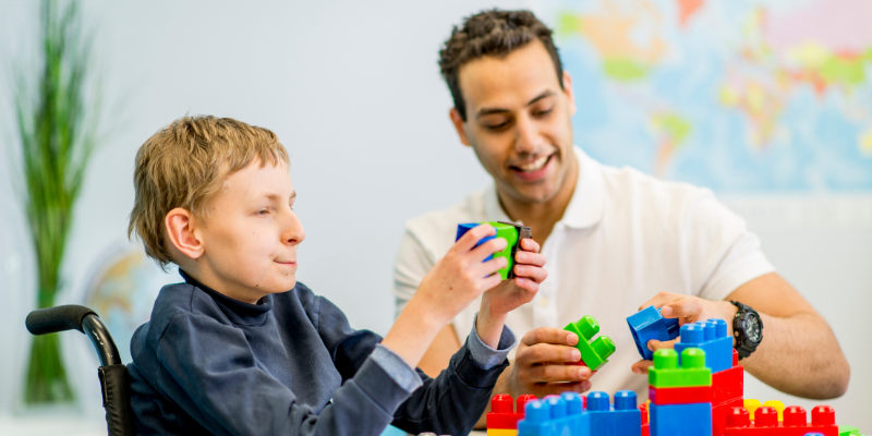 Young boy in wheelchair playing with building blocks with smiling man next to him