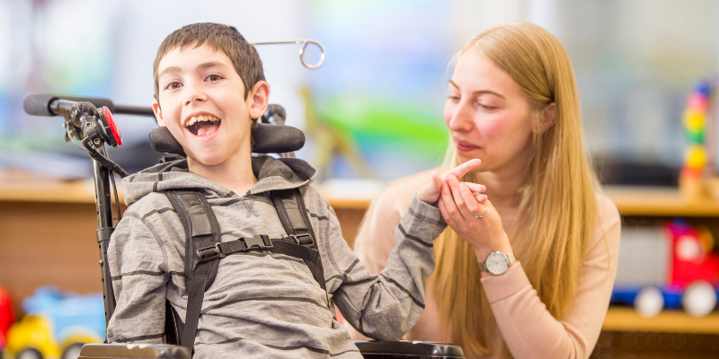 Boy with disability smiling in wheelchair with woman next to him smiling