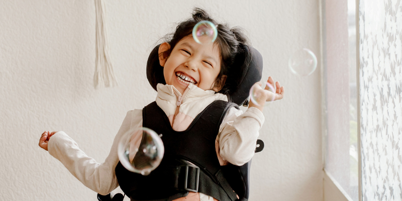 Young girl in wheelchair smiling with bubbles floating in front of her