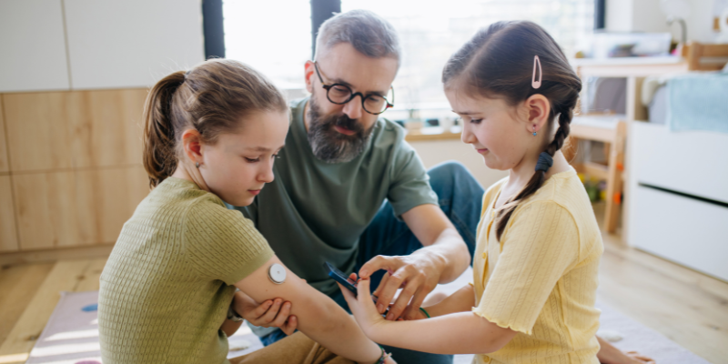 Daughter helping father check her sister's blood glucose levels with smartphone held to the CGM on the back of the arm