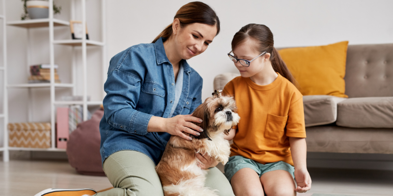 Mom and daughter sitting on the floor together holding onto their dog