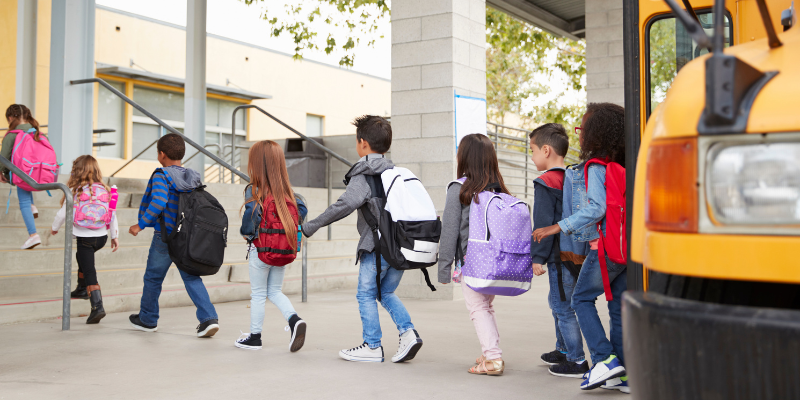 School kids with backpacks getting off the bus and walking toward school