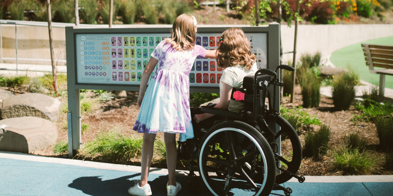 Girl in wheelchair with another girl at the park