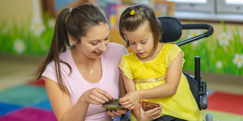 Smiling woman playing cards with child in wheelchair